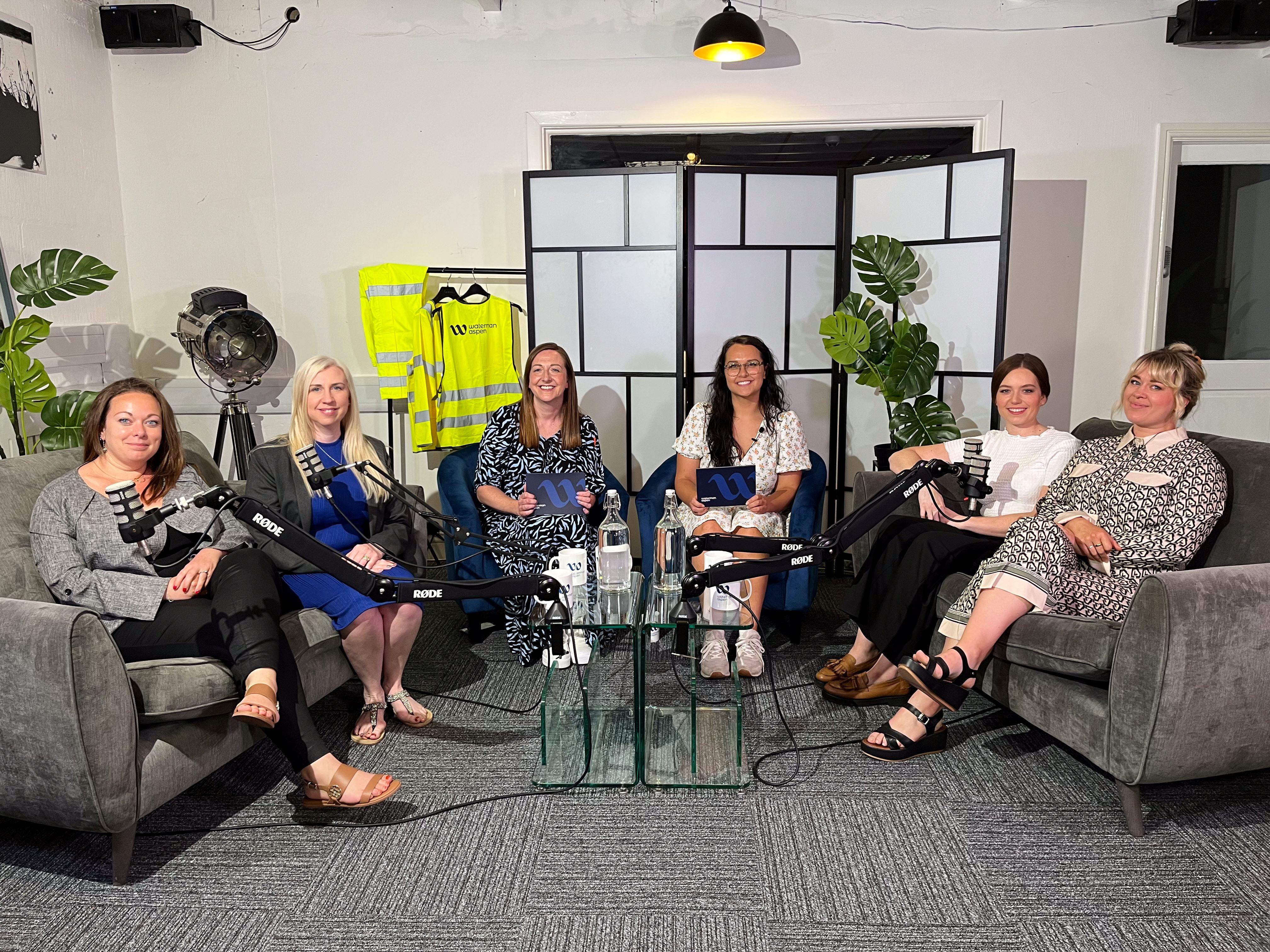 Panel of women sat on grey sofa's infront of podcast microphones